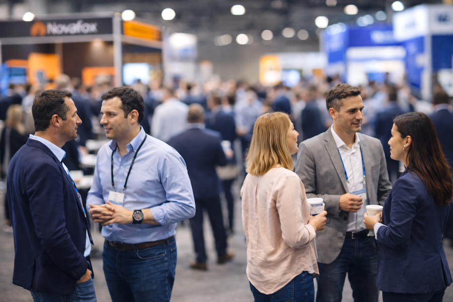 Professionals networking at an IT lifecycle industry conference with exhibition booths in the background